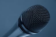 A detailed close-up of a microphone with a blue monochrome background, highlighting its intricate mesh design.